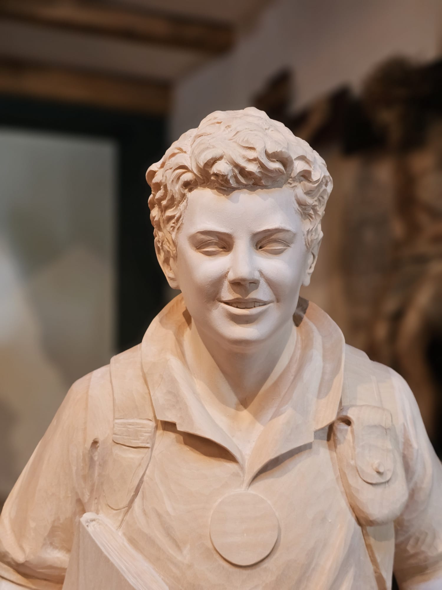 Fertige Statue von Carlo Acutis, die ihn mit einem Rucksack auf dem Rücken zeigt. In einer Hand hält er eine Bibel und einen Rosenkranz, in der anderen einen Camcorder. Ein Hund sitzt am Boden neben ihm und schaut ihn an, während Carlo einen Fuß auf einem Fußball hat. Diese Statue wurde von der Schreinerei Ferdinand Stuflesser unter der Leitung von Robert Stuflesser erschaffen.
