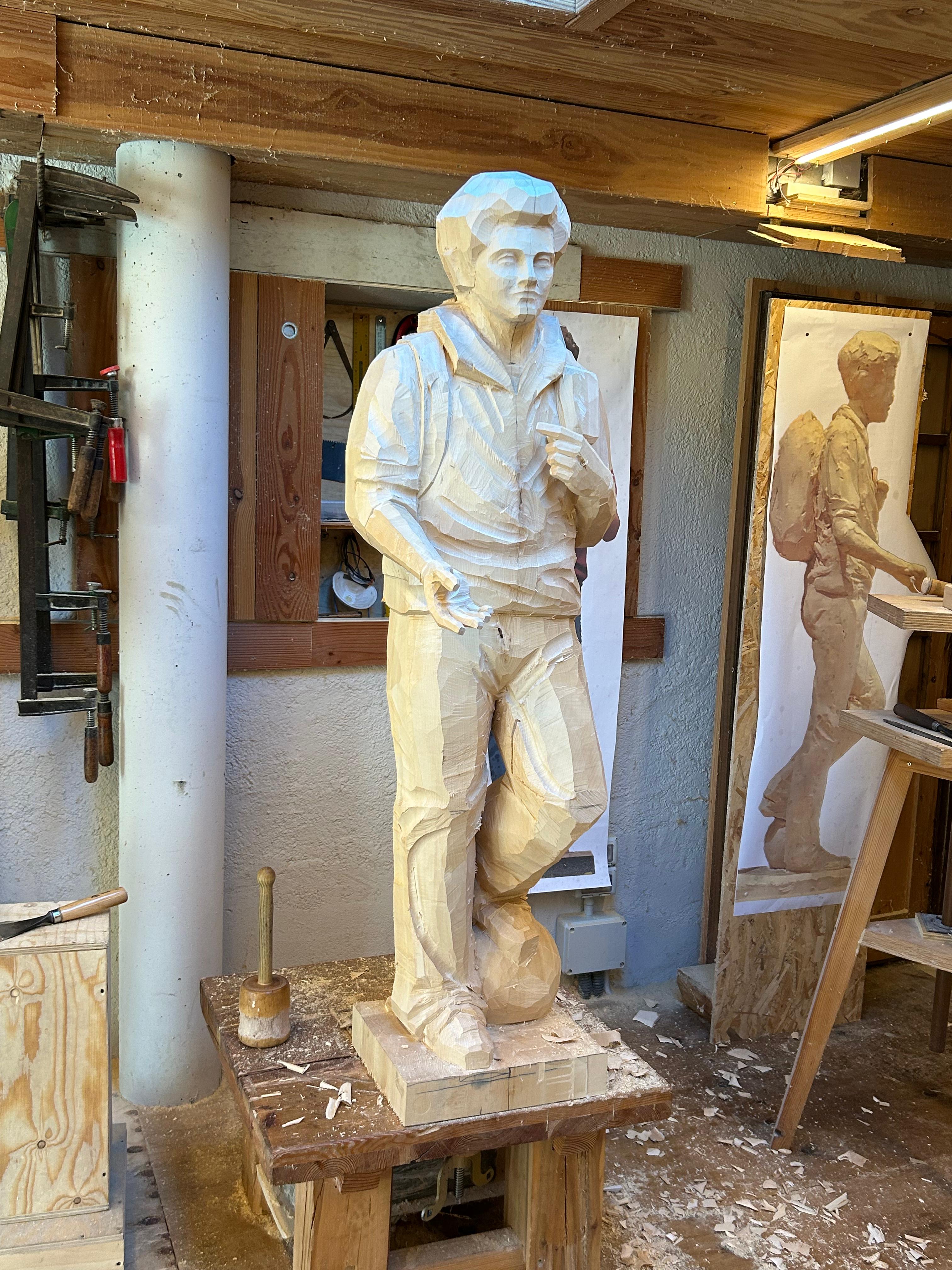 Detailaufnahme des fortgeschrittenen Prozesses der Carlo Acutis Statue, die ihn mit einem Bein auf einem Fußball und einem Rucksack darstellt. Das Bild zeigt die feineren Details der Statue, die noch in unbemalter Form ist, aber bereits die Form und Haltung von Carlo deutlich erkennen lässt. Die Statue wurde von der Schreinerei Ferdinand Stuflesser unter der Leitung von Robert Stuflesser gefertigt.